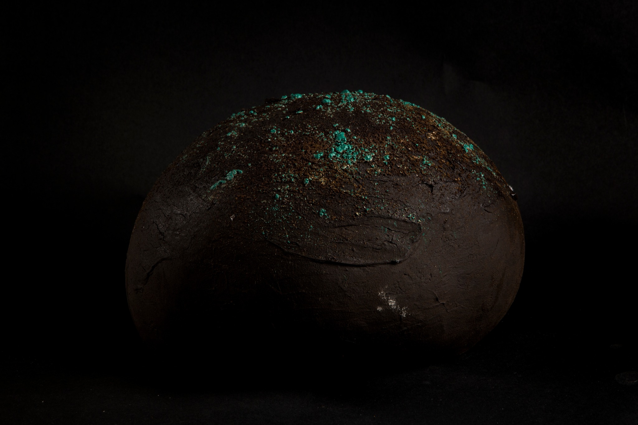 Peça ceràmica negra amb textura mineral i punts verds sobre fons negre